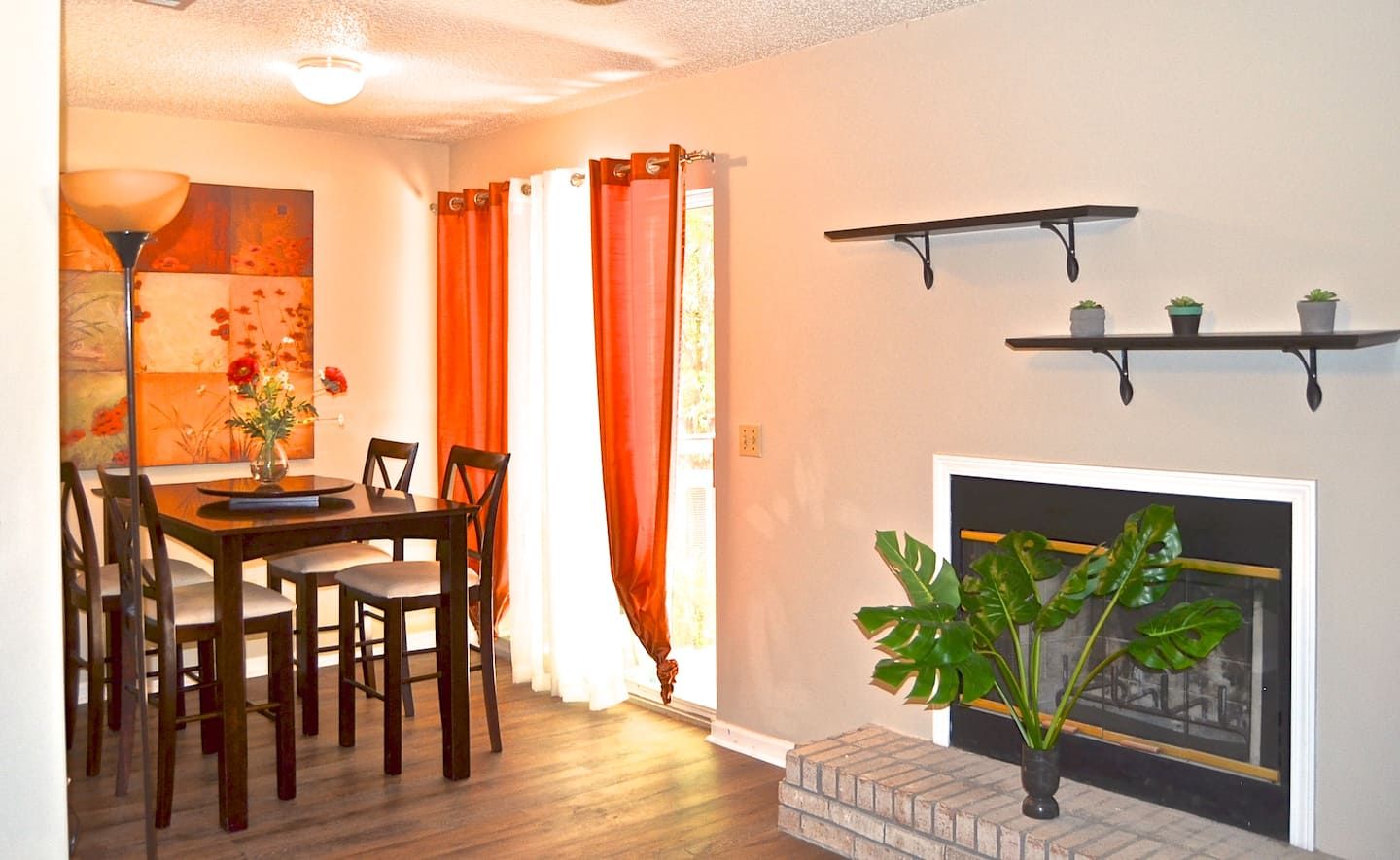 Un comedor con una mesa y sillas de madera, una chimenea y dos estantes empotrados con plantas.