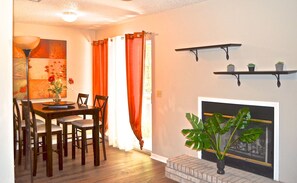 Un comedor con una mesa y sillas de madera, una chimenea y dos estantes empotrados con plantas.