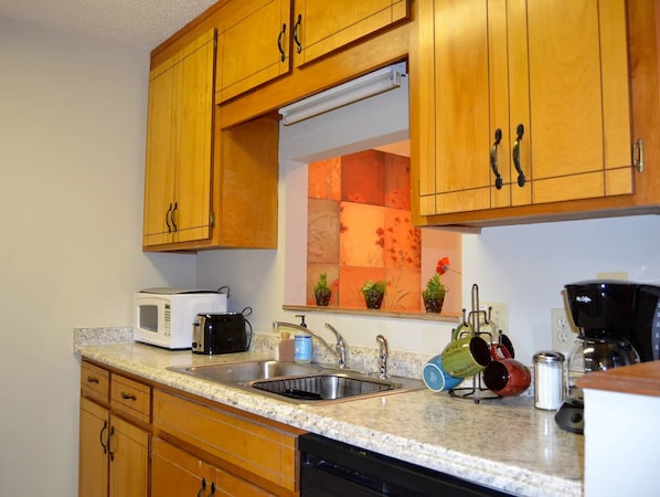 Una cocina con armarios de madera, microondas, cafetera y lavabo.