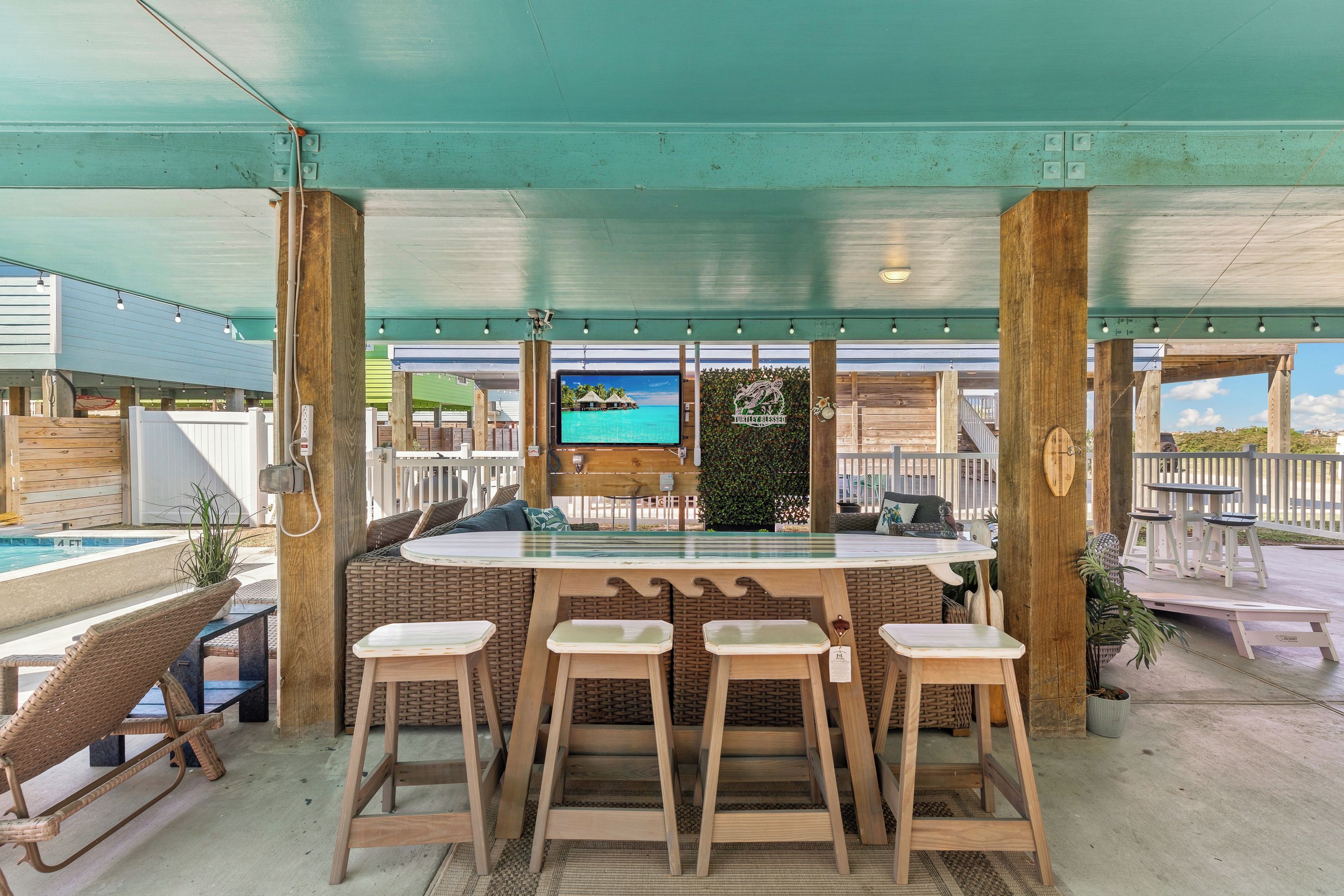 A covered outdoor bar area with a pool view, wooden stools, and a television screen.