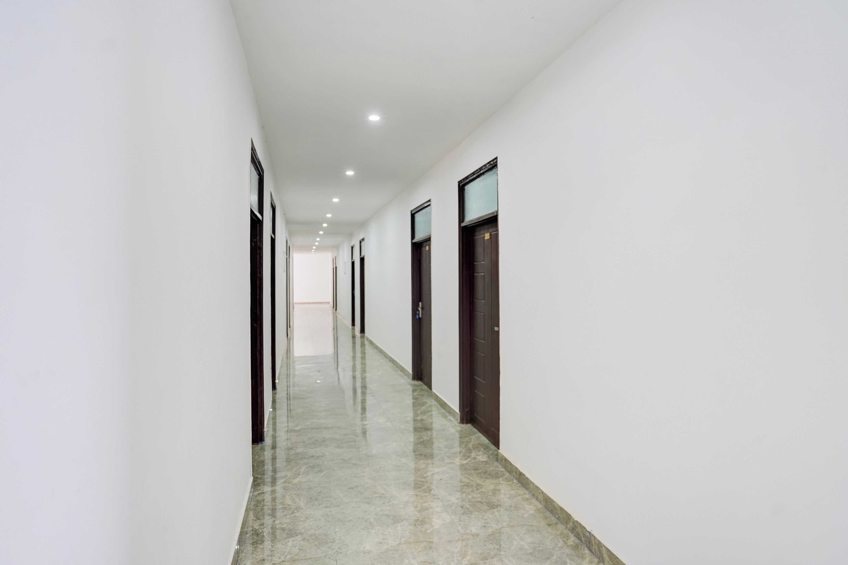 Un pasillo largo y estrecho con puertas a ambos lados, que conduce a una habitación luminosa al final.