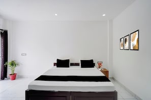 Een hotelkamer met een groot bed, een nachtkastje, een potplant en wanddecoratie.