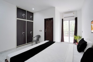 Een slaapkamer met een bed, een kledingkast, een stoel, een raam met gordijnen en een kamerplant.