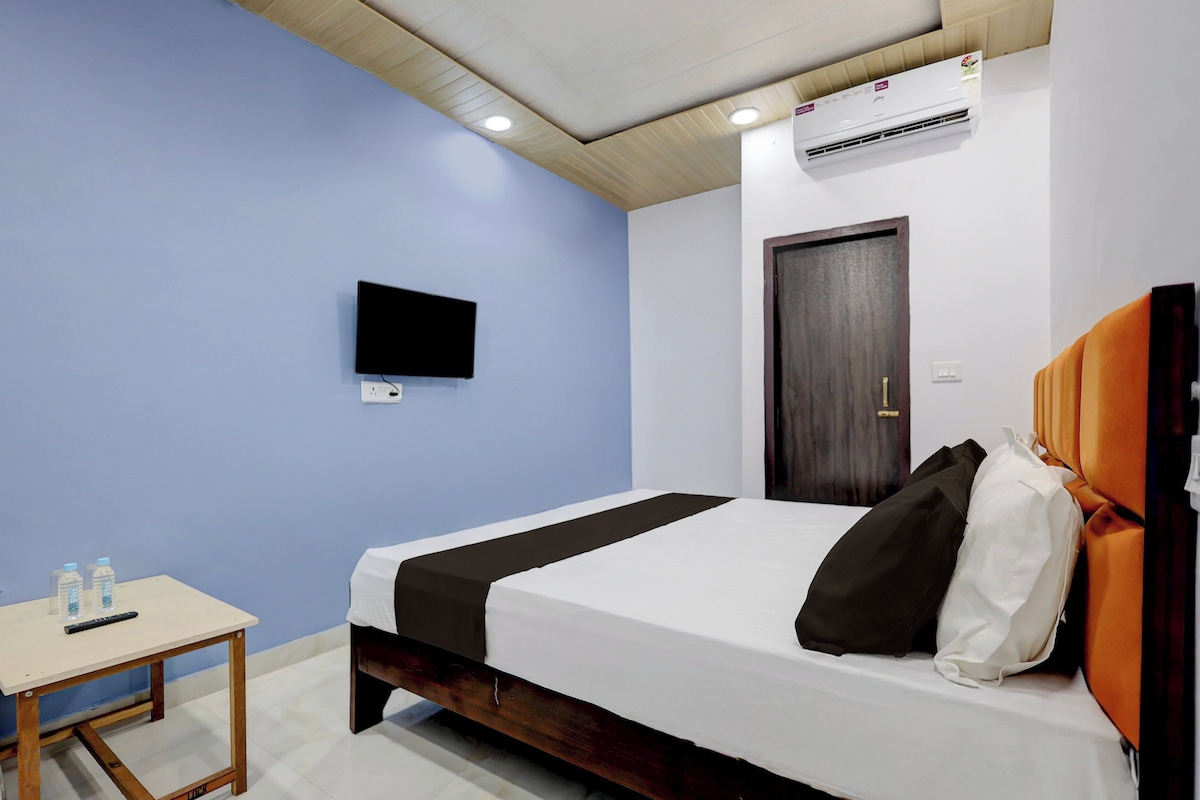 A hotel room with a bed, a television on the wall, and an air conditioning unit.