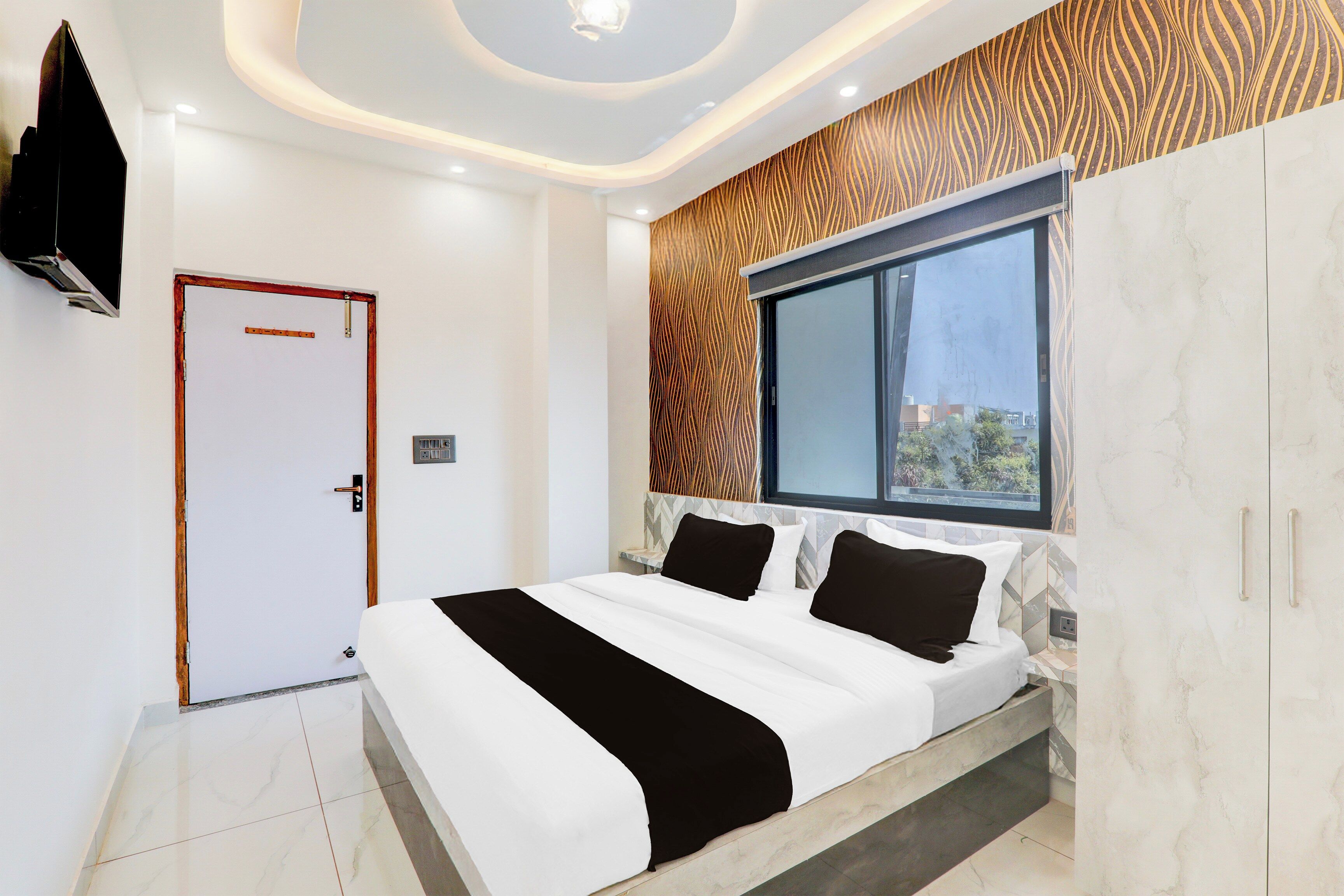 Un dormitorio moderno con una cama grande, una ventana con vistas, una puerta y un televisor montado en la pared.