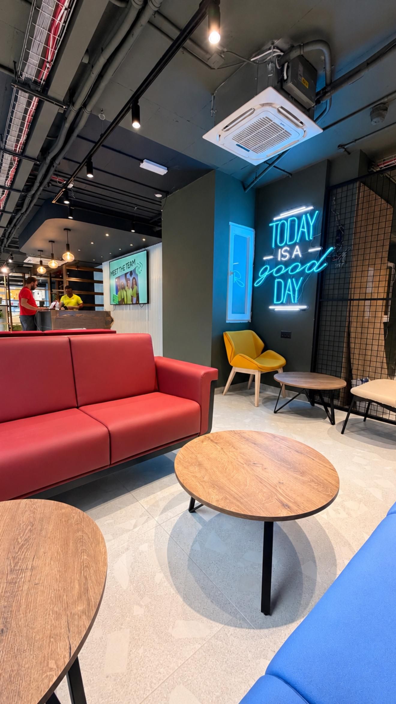 A modern lounge area with a red sofa, wooden tables, and a neon sign that reads 'TODAY IS A GOOD DAY.'