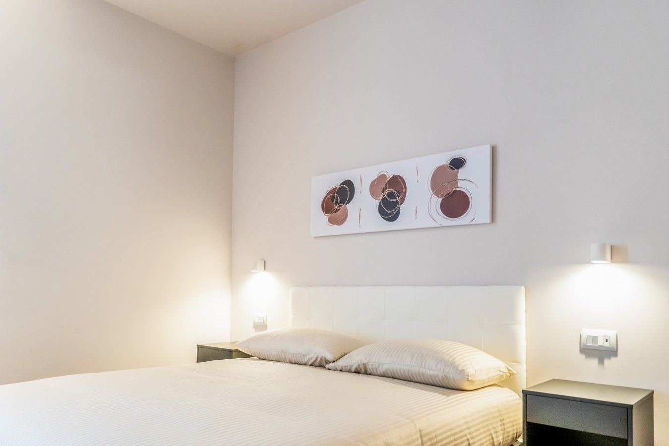 Ein Schlafzimmer mit einem Bett, zwei Nachttischlampen und einem an der Wand hängenden, abstrakten Kunstwerk.