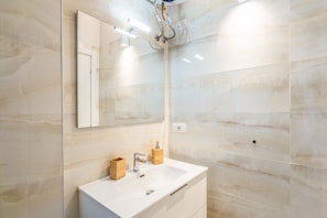 Un baño moderno con tocador blanco, espejo y ducha.
