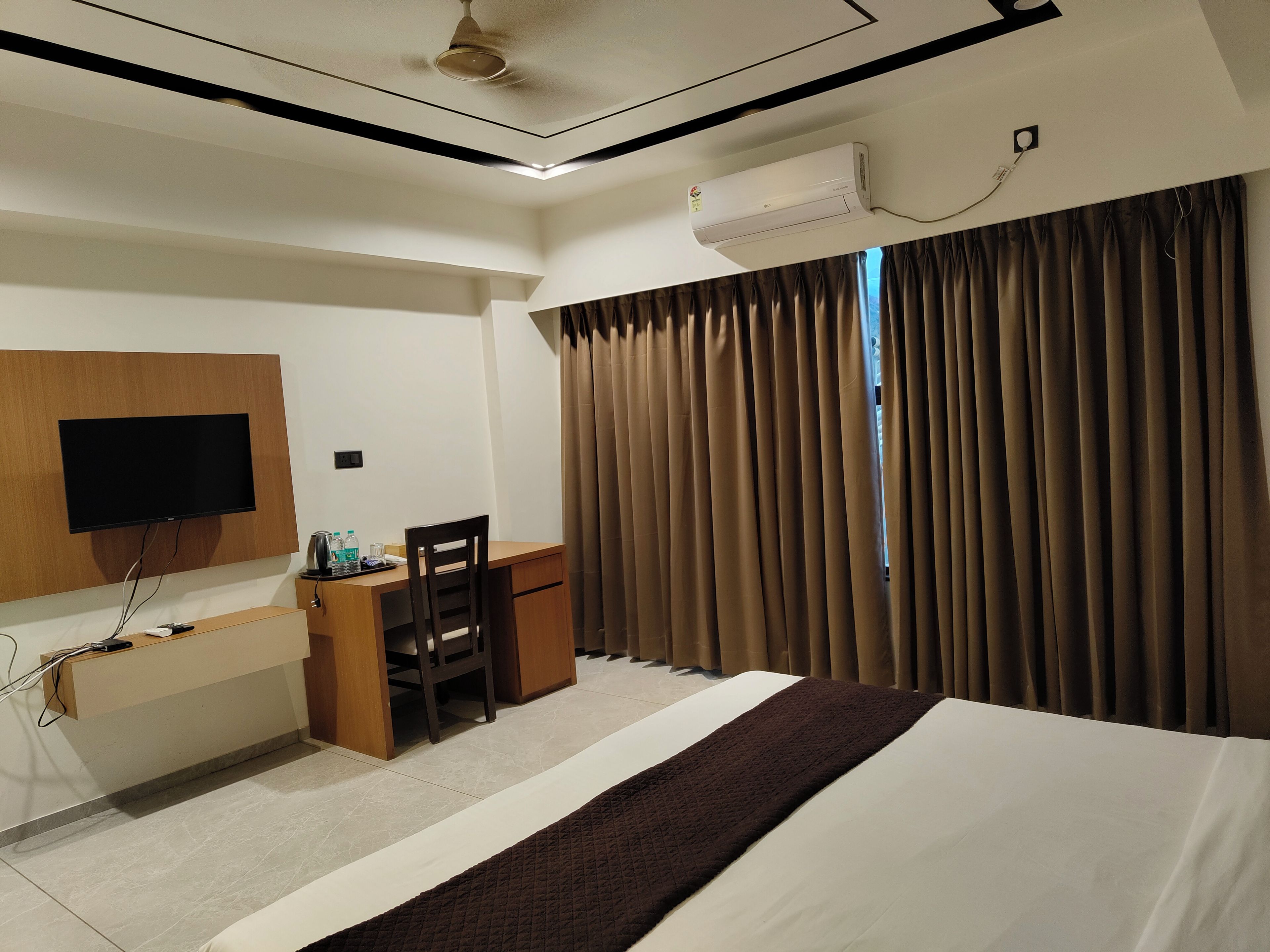 Une chambre d’hôtel équipée d’un lit, d’un bureau, d’une chaise, d’un téléviseur à écran plat et d’une fenêtre avec des rideaux.