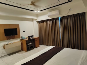 Habitación de hotel con cama, escritorio, silla, televisor de pantalla plana y ventana con cortinas.