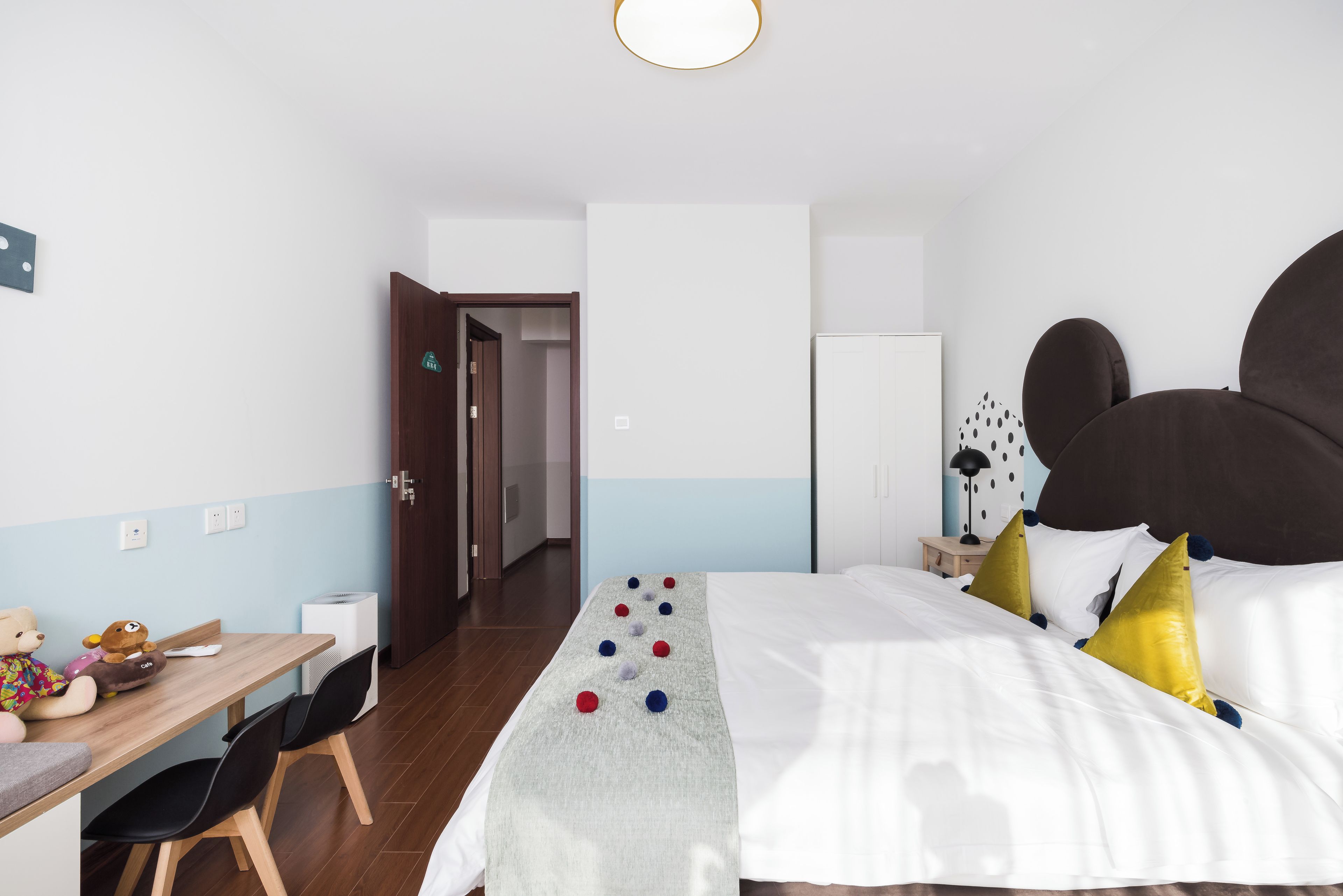 Una habitación de hotel con cama, mesita de noche, silla y escritorio con un peluche de oso.