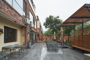 Un patio con mesas al aire libre, un adorno con forma de barco de madera y una zona cubierta con sombrillas.