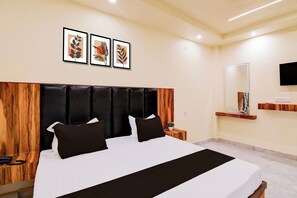 A hotel room with a large bed, a wooden headboard, a bedside table with a phone, and a wall-mounted TV. - Hotel O Pinaki House (Lucknow)