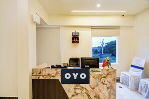 A reception desk with a sign reading 'OYO' and a window with a view of trees and power lines. - Hotel O Pinaki House (Lucknow)
