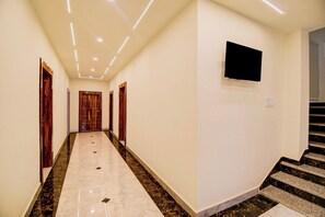 A hotel hallway with a marble floor, wooden doors, and a flat-screen TV mounted on the wall. - Hotel O Pinaki House (Lucknow)