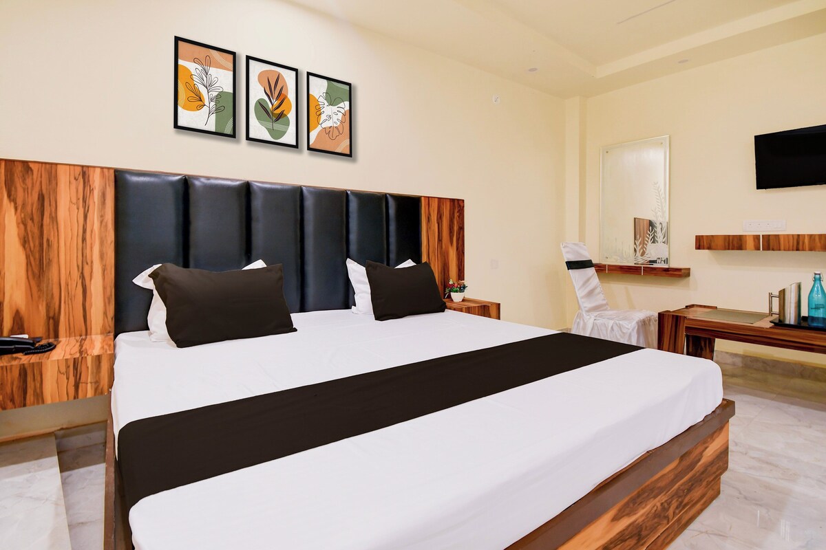 A hotel room with a large bed, a wooden headboard, a flat-screen TV mounted on the wall, and artwork above the bed.
