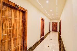 A hallway with wooden doors and a marble floor. - Hotel O Pinaki House (Lucknow)