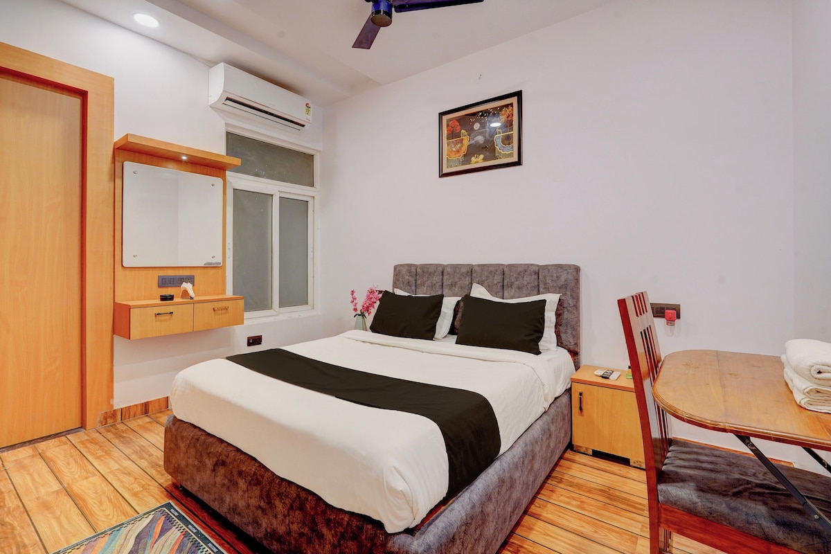 Une chambre d’hôtel avec un lit, une table de chevet, une chaise, une fenêtre, un appareil de climatisation et un tableau au mur.