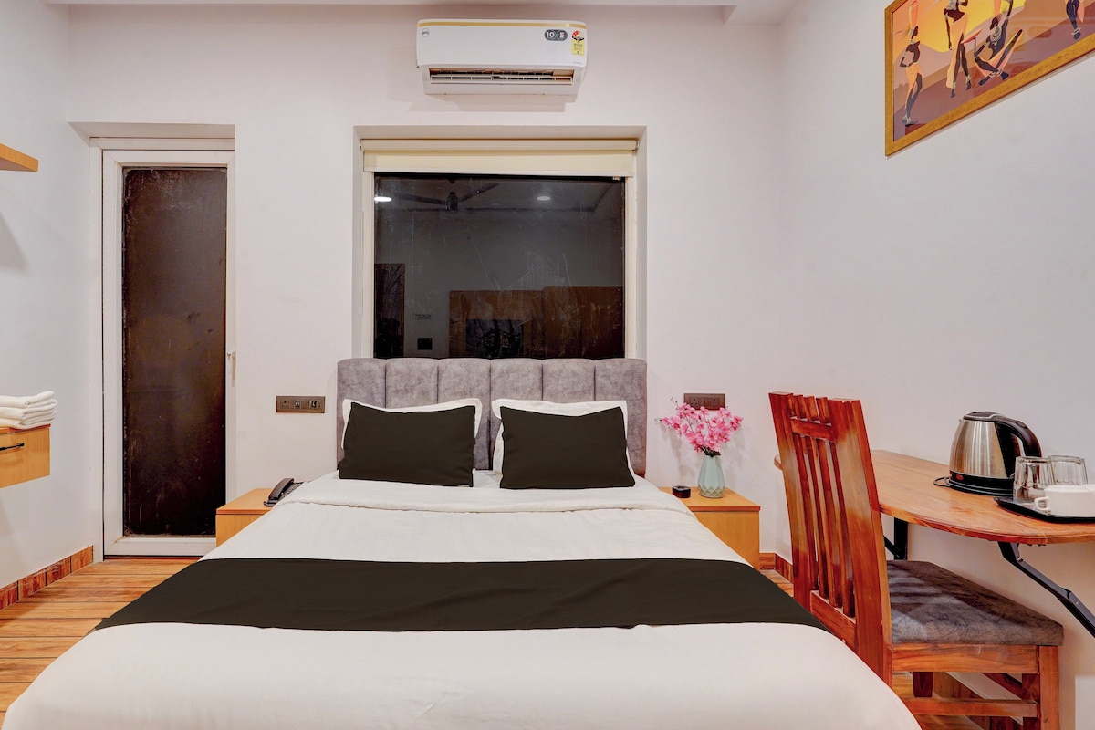 A hotel room with a bed, a desk with a chair, a window, and an air conditioning unit.