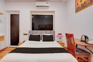 A hotel room with a bed, a desk with a chair, a window, and an air conditioning unit. - Hotel O Grand Crown (Lucknow)