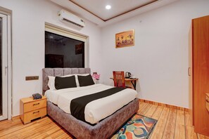 A hotel room with a bed, bedside table, nightstand, and a window with an air conditioning unit. - Hotel O Grand Crown (Lucknow)