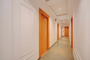 Un long couloir étroit aux murs blancs et aux portes en bois, qui mène à une pièce au fond.