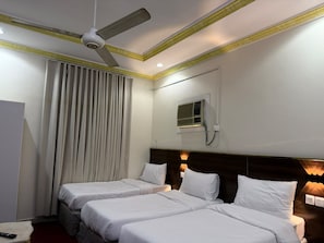 Habitación de hotel con dos camas, ventilador de techo, ventana con persianas y aire acondicionado de pared.