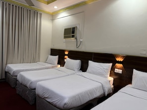 A hotel room with three beds, a window with curtains, an air conditioning unit, and wall-mounted lights. - Noor Al-Salam 2 Hotel, Gemmayzeh (Makkah Al-Mukarramah)