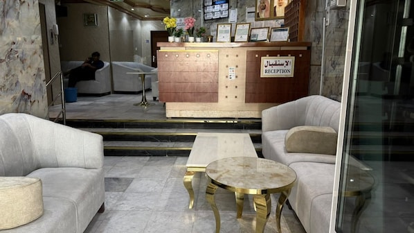 Un área de recepción con una mesa de recepción, dos sofás, una mesita de centro y una persona sentada al fondo.