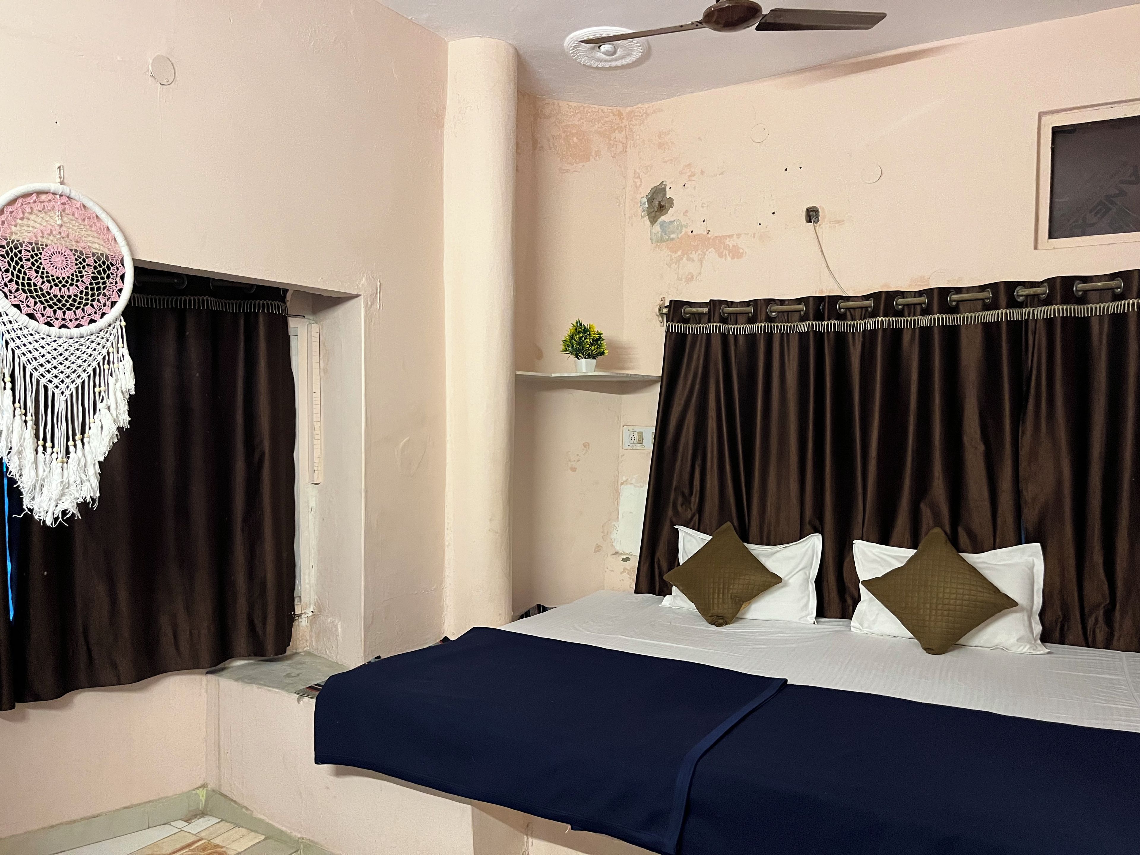 A bedroom with a bed, curtains, a ceiling fan, and a wall-mounted shelf with a plant.