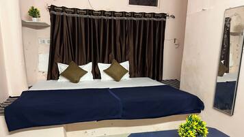 A bedroom with a bed, a bedside table with a plant, a mirror, and a curtain.
