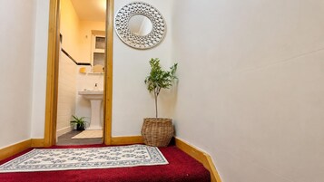 A hallway with a red carpet, a potted plant, a wicker basket, and a wall-mounted mirror.