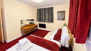 Quarto de hotel com cama, cômoda de madeira, espelho, TV de tela plana e cortina vermelha.