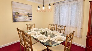 Uma sala de jantar com mesa de vidro, seis cadeiras e um quadro na parede.