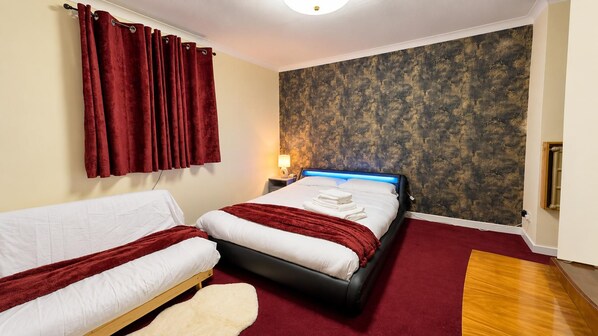 Quarto de hotel com cama, sofá, tapete vermelho e parede texturizada.