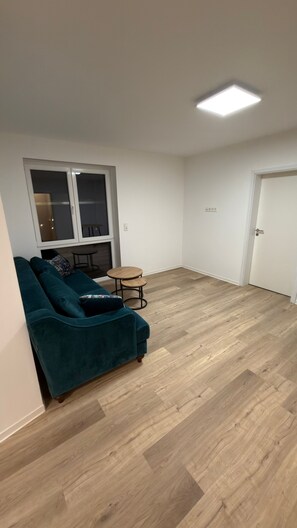 Um quarto com um sofá verde-água, uma mesa redonda pequena e uma porta.