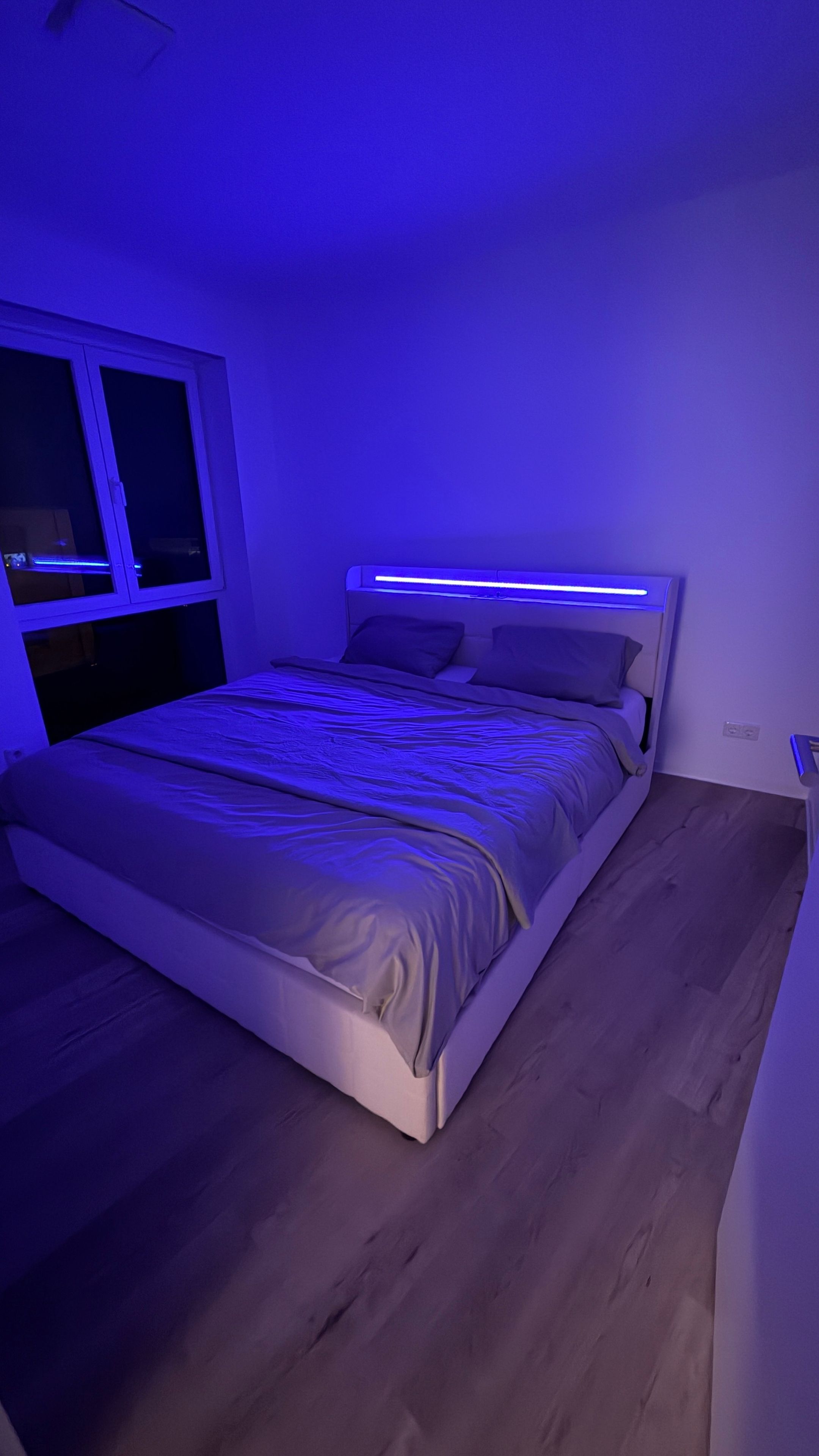 A bedroom with a bed, a window, and a wall-mounted light fixture.