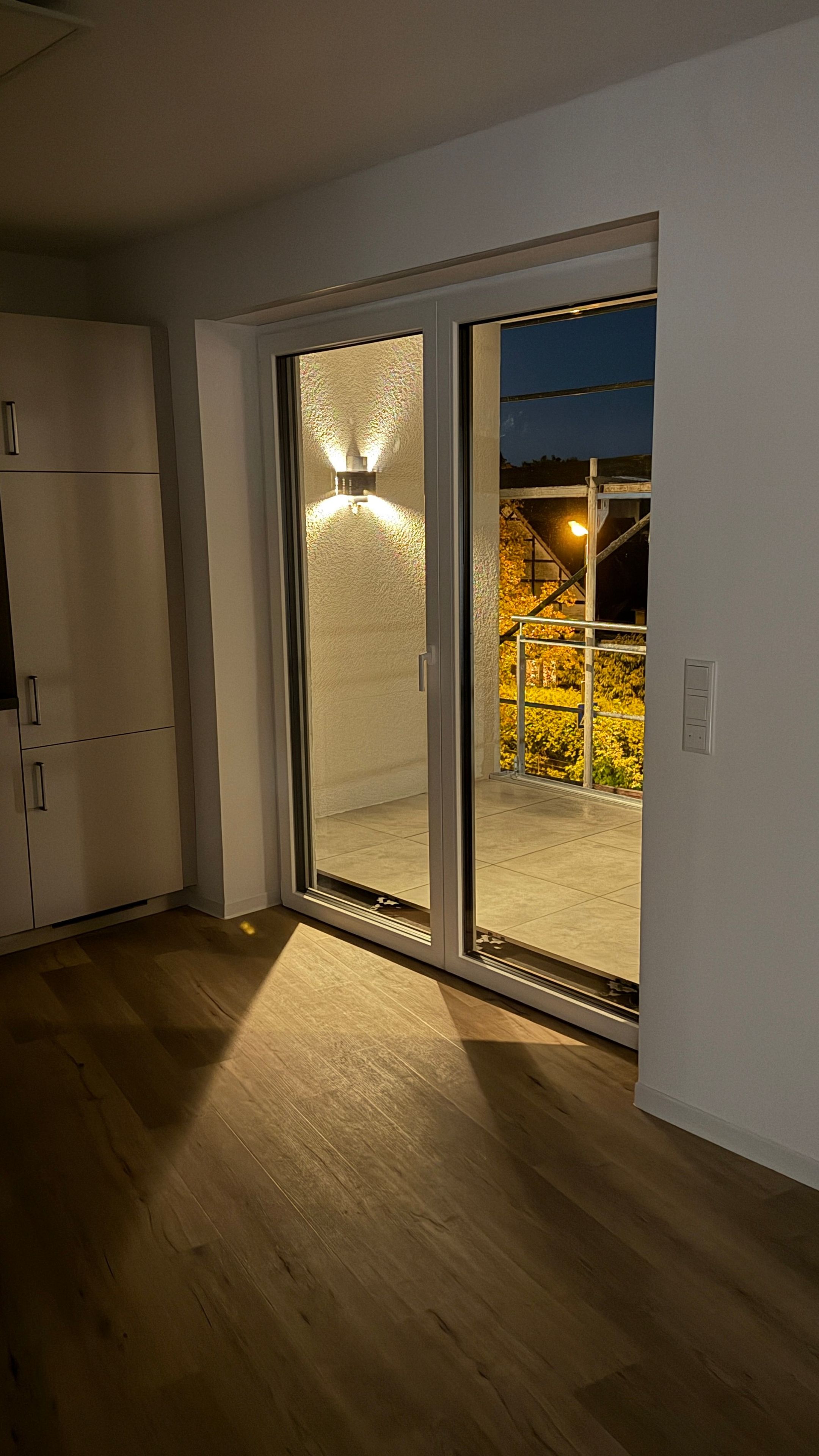 Habitació amb porta corredissa de vidre que dona a zona exterior, terra de fusta i paret blanca.