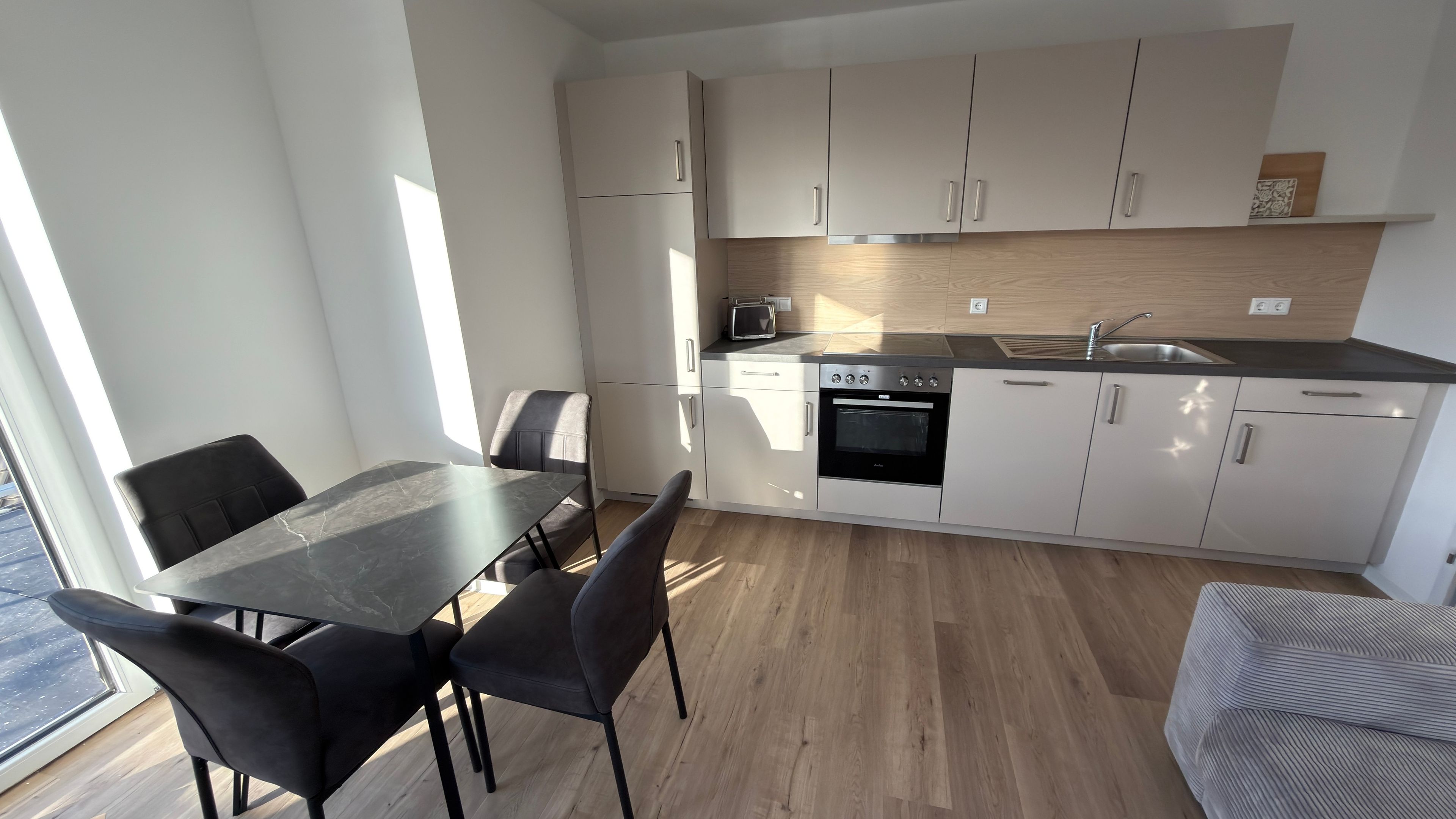 A modern kitchen with white cabinets, a black countertop, and a dining area with a table and chairs.