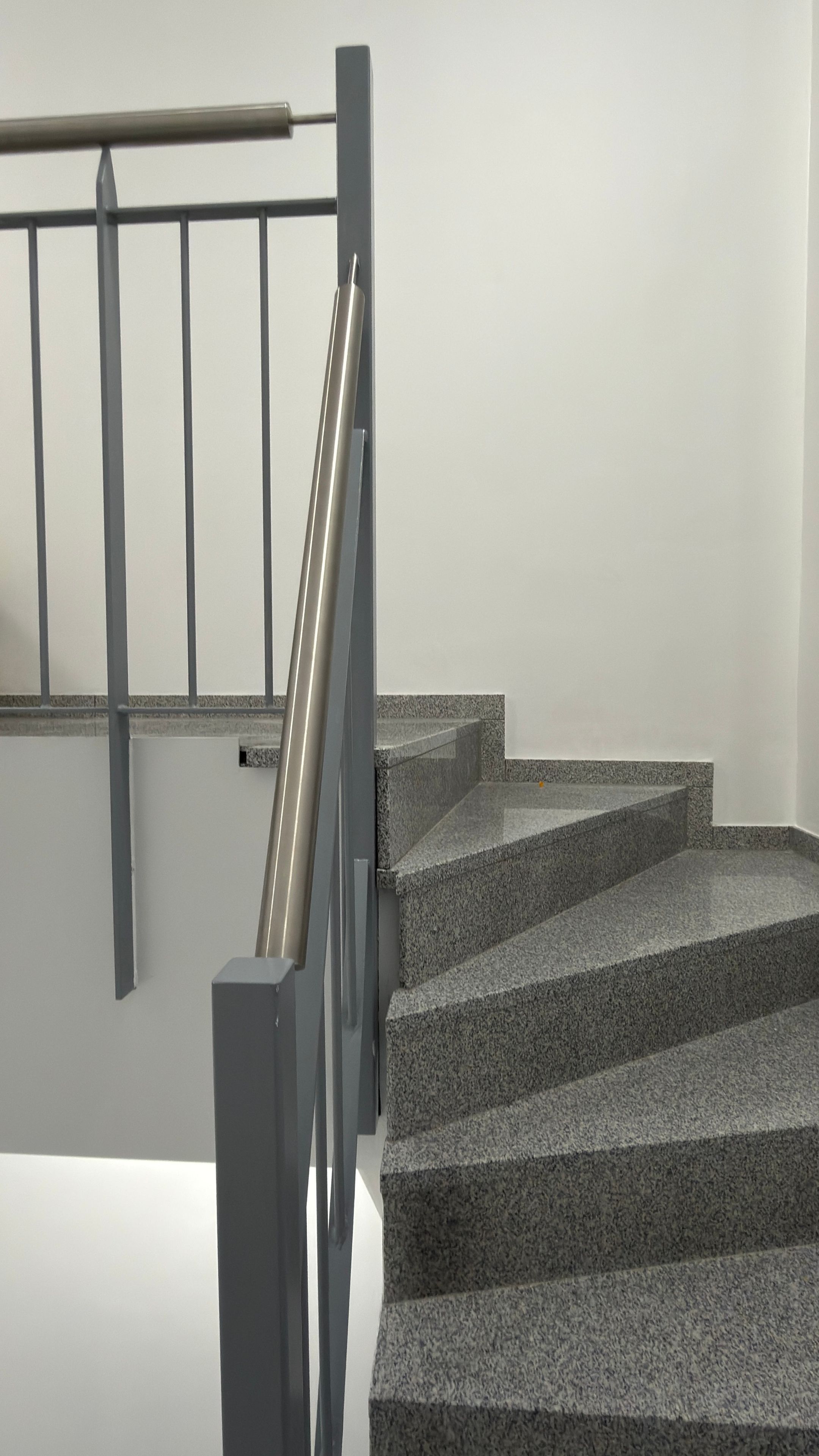 Un escalier avec une rampe métallique et des marches en granit.