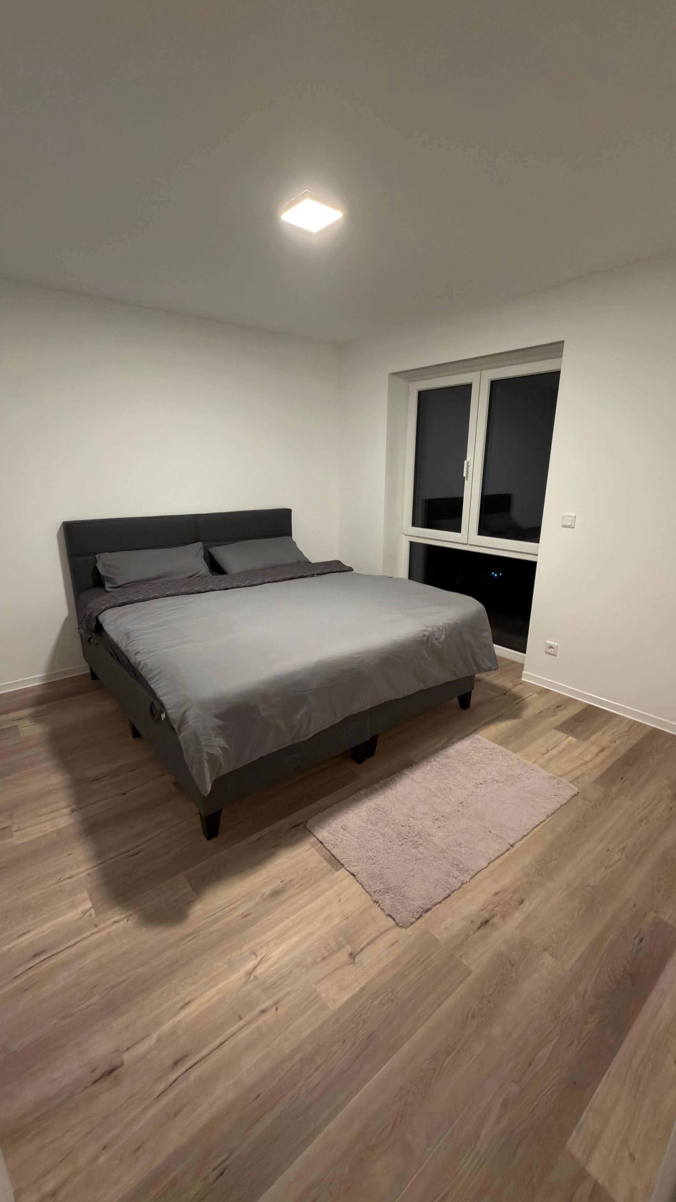 Un dormitorio con cama, ventana y lámpara en el techo.