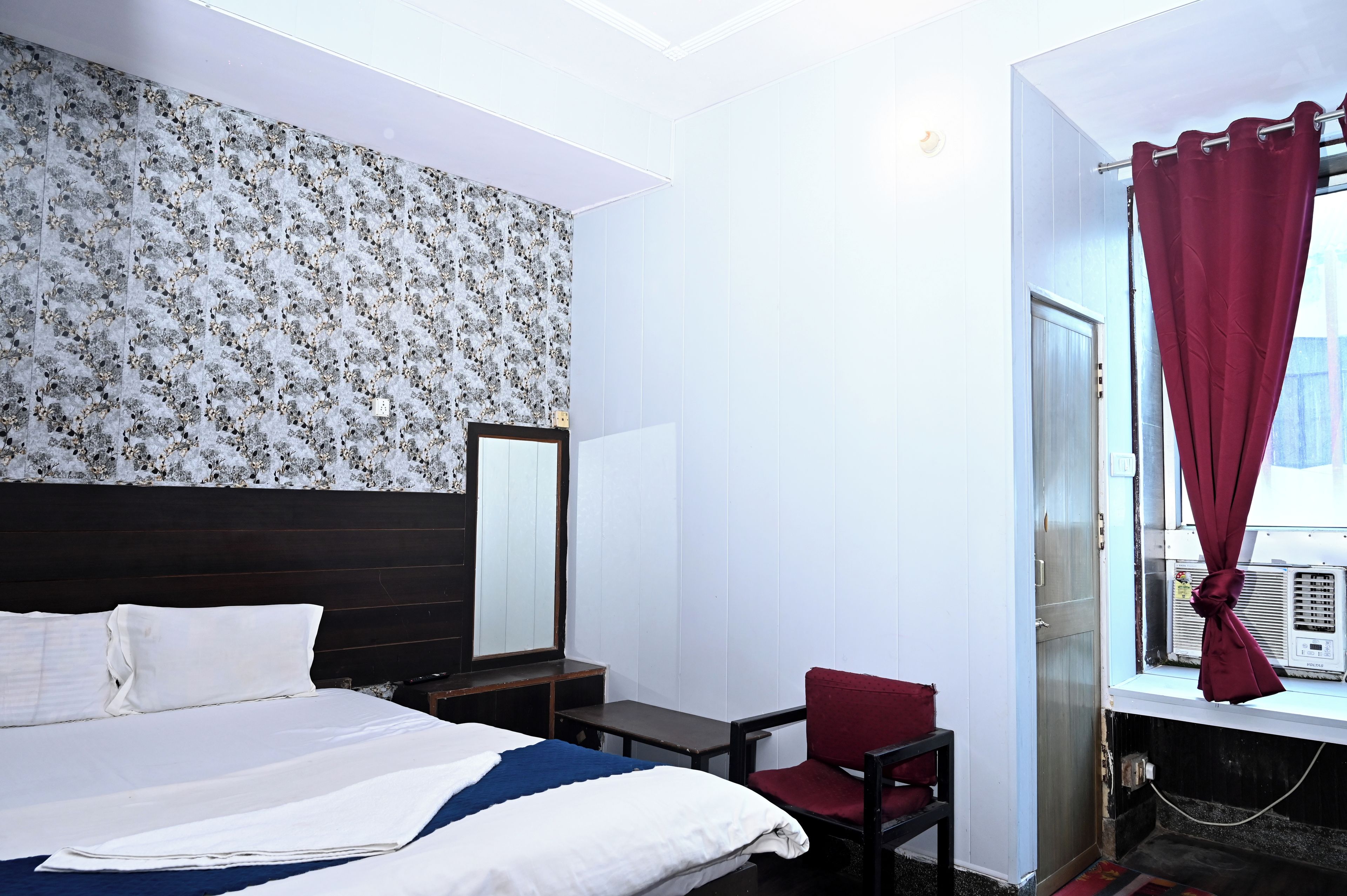 A hotel room with a bed, a chair, a desk, a mirror, and a window with curtains.
