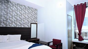 A hotel room with a bed, a chair, a desk, a mirror, and a window with curtains.