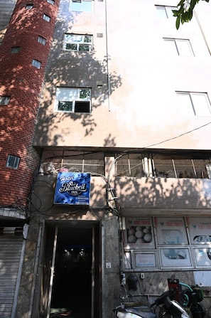 A building with a blue sign for Hotel Bluebell Inn, a brick tower, and a garage door with a motorcycle parked outside. - Hotel Bluebell one by M.B. Hotel Resorts (Lucknow)