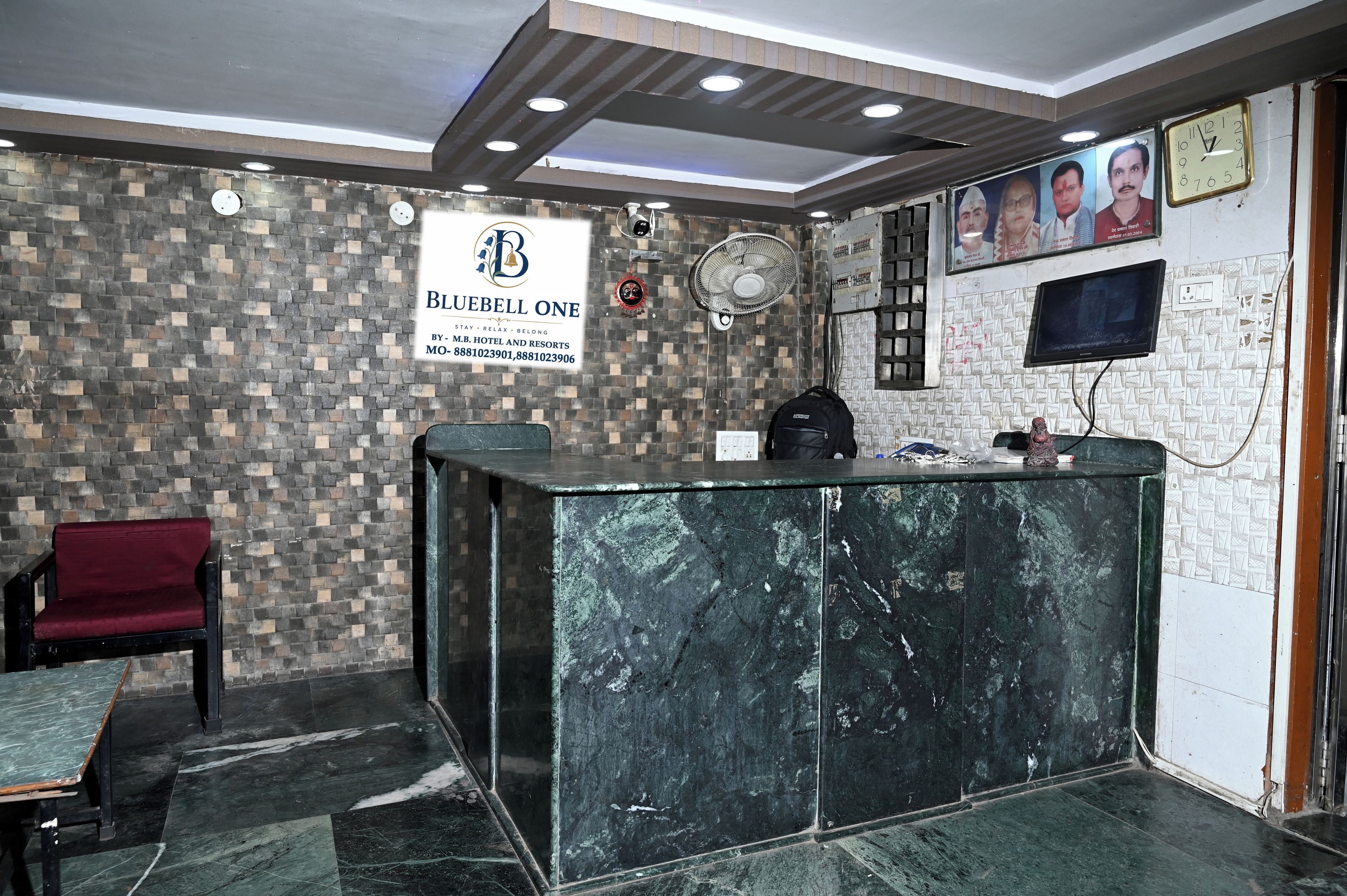 A reception area with a marble reception desk, a red chair, a wall-mounted fan, and a clock.