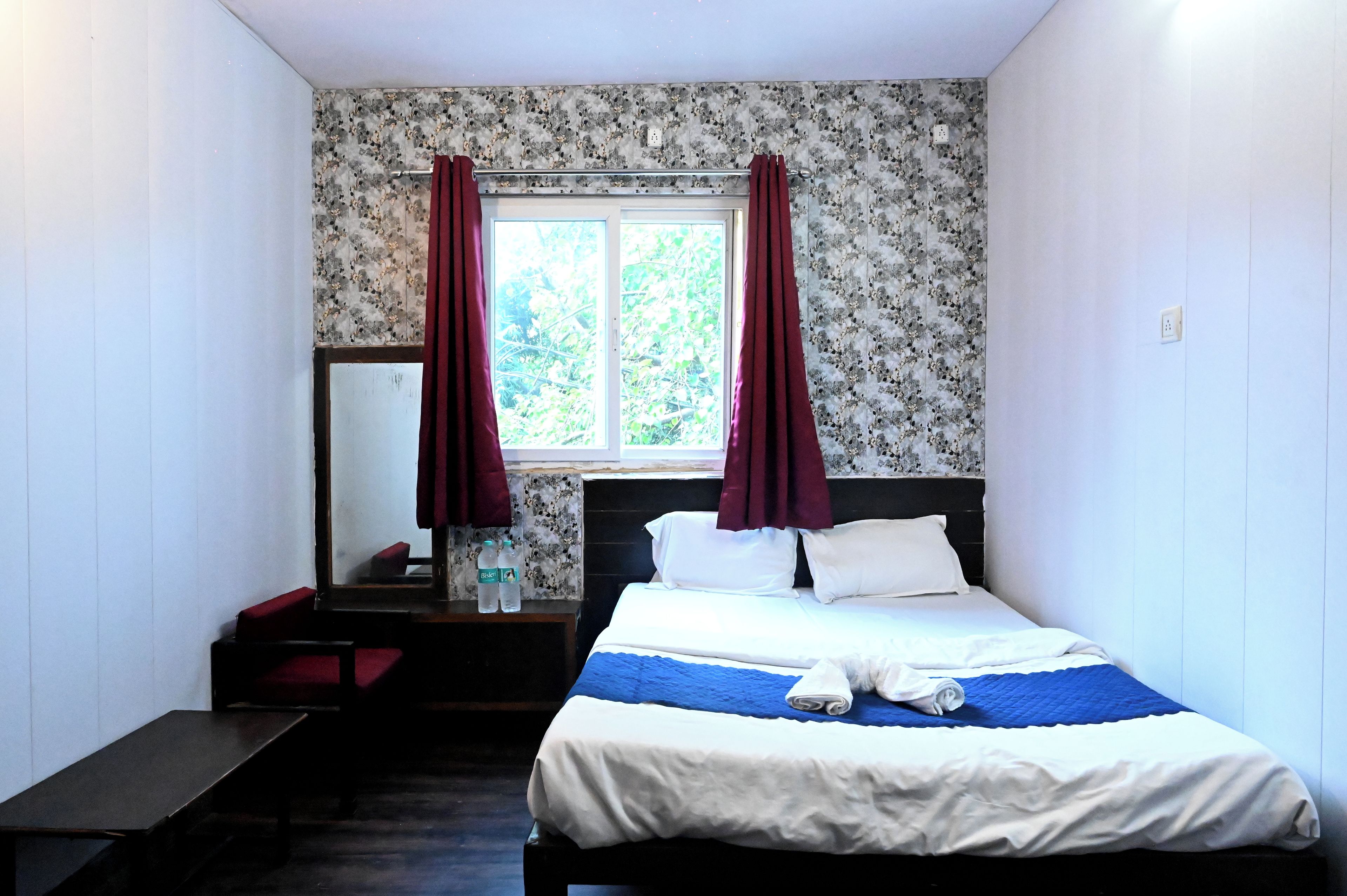 A bedroom with a bed, a desk, a mirror, and a window with curtains.