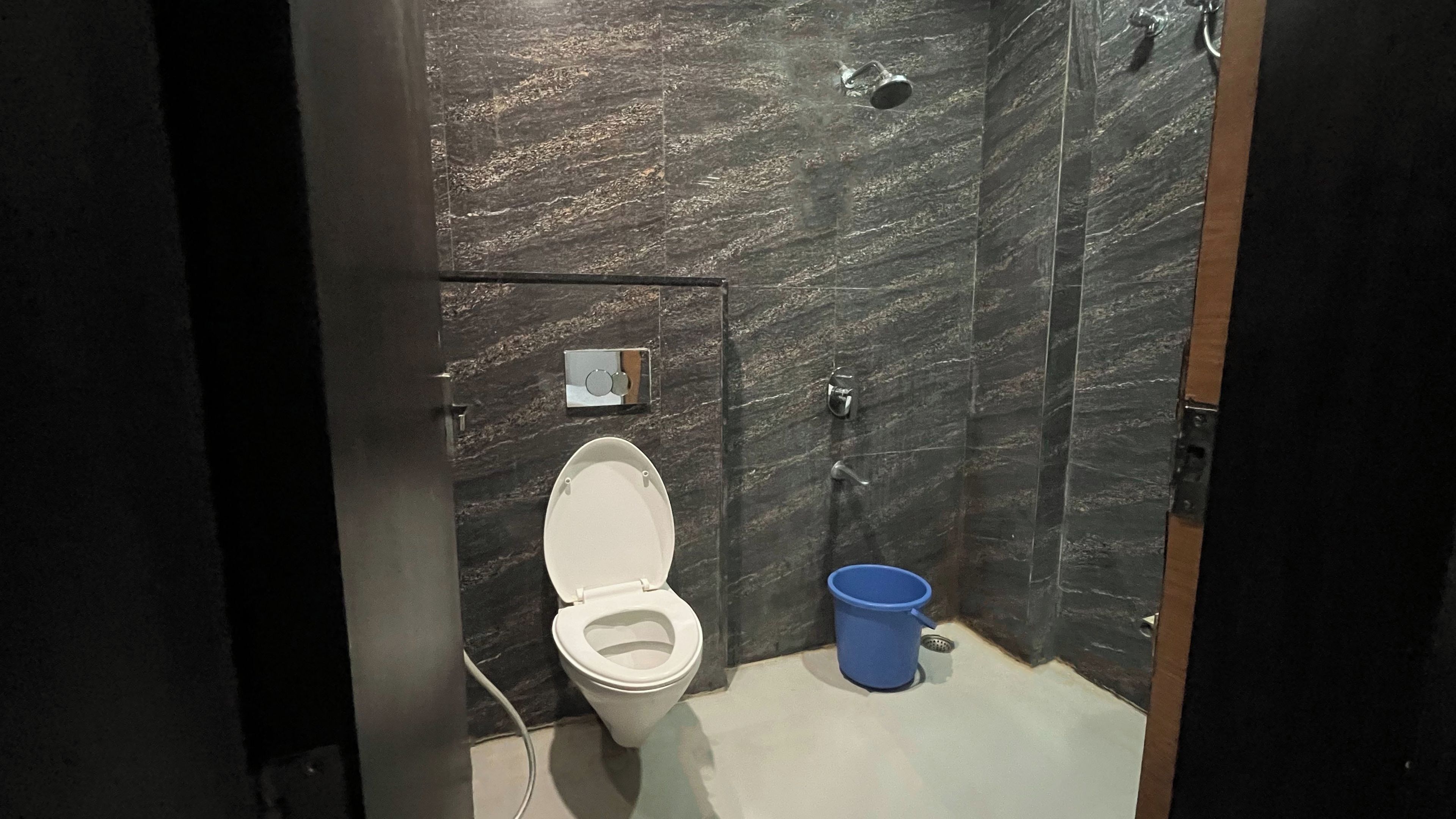 Un baño moderno con inodoro blanco, un cubo azul y una zona de ducha.