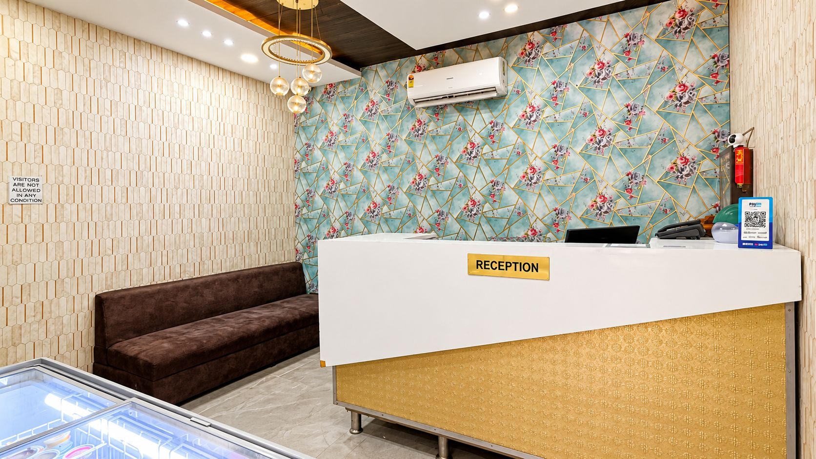 A reception area with a reception desk, a brown sofa, a patterned wall, and a ceiling light fixture.
