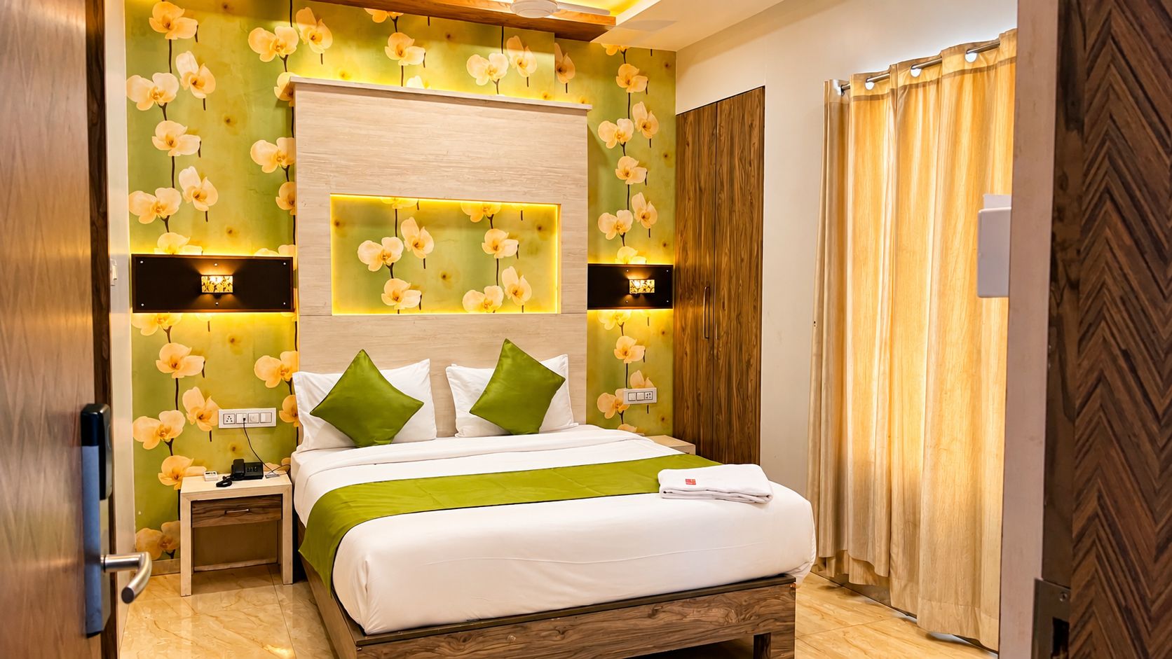 Ett hotellrum med en säng, sängbord, en sänggavel i trä och en vägg med blommig tapet.