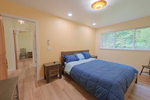 Um quarto com uma cama, mesas de cabeceira, uma janela e uma porta que dá para outro cômodo.